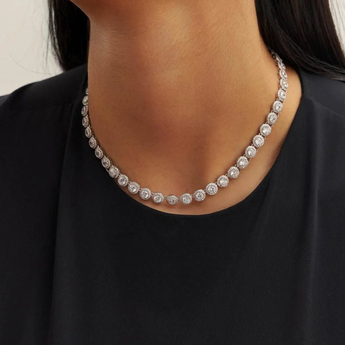 Modelo vestindo blusa preta usando Colar Riviera banhado no ródio com zircônias redondas rente ao pescoço.
